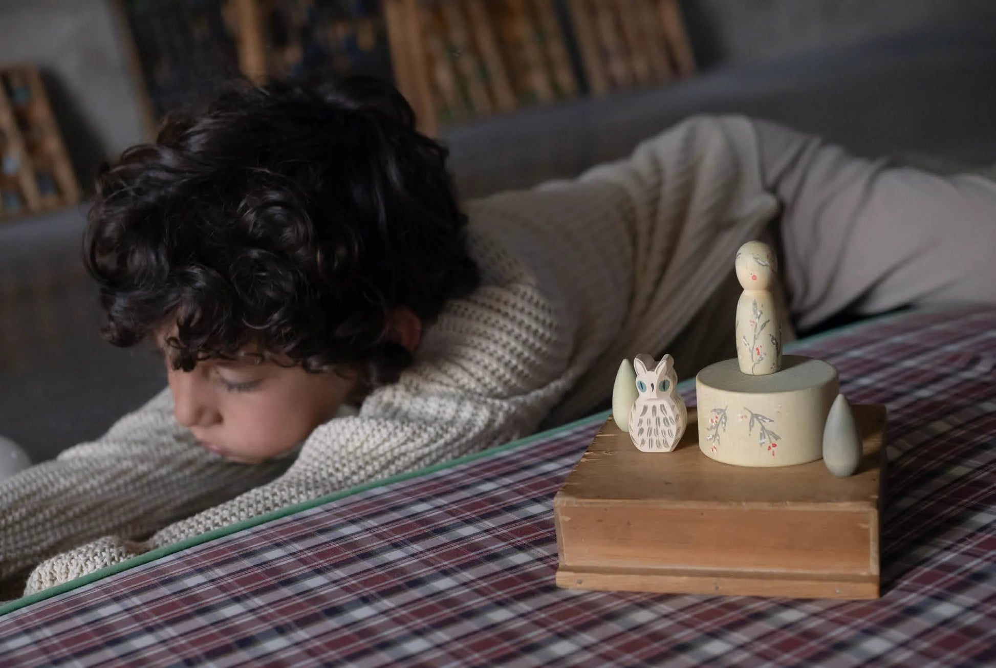 Child lying on a bed with wooden figurines on a table in the foreground